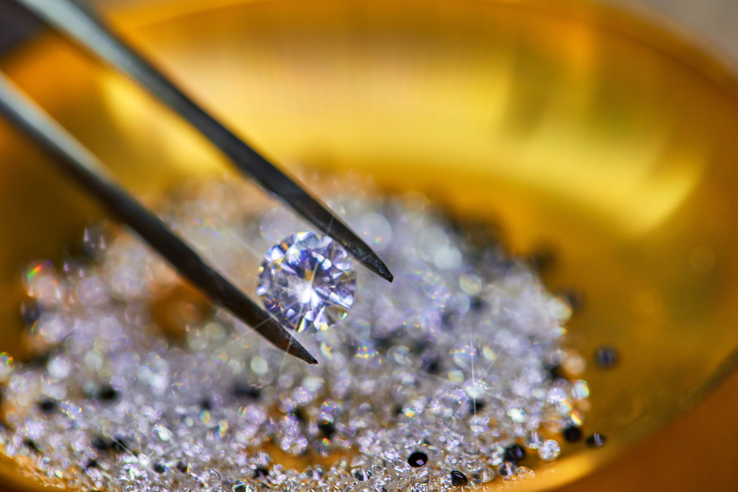 Diamond held by tweezers against the background of diamonds in the plate for the fixer