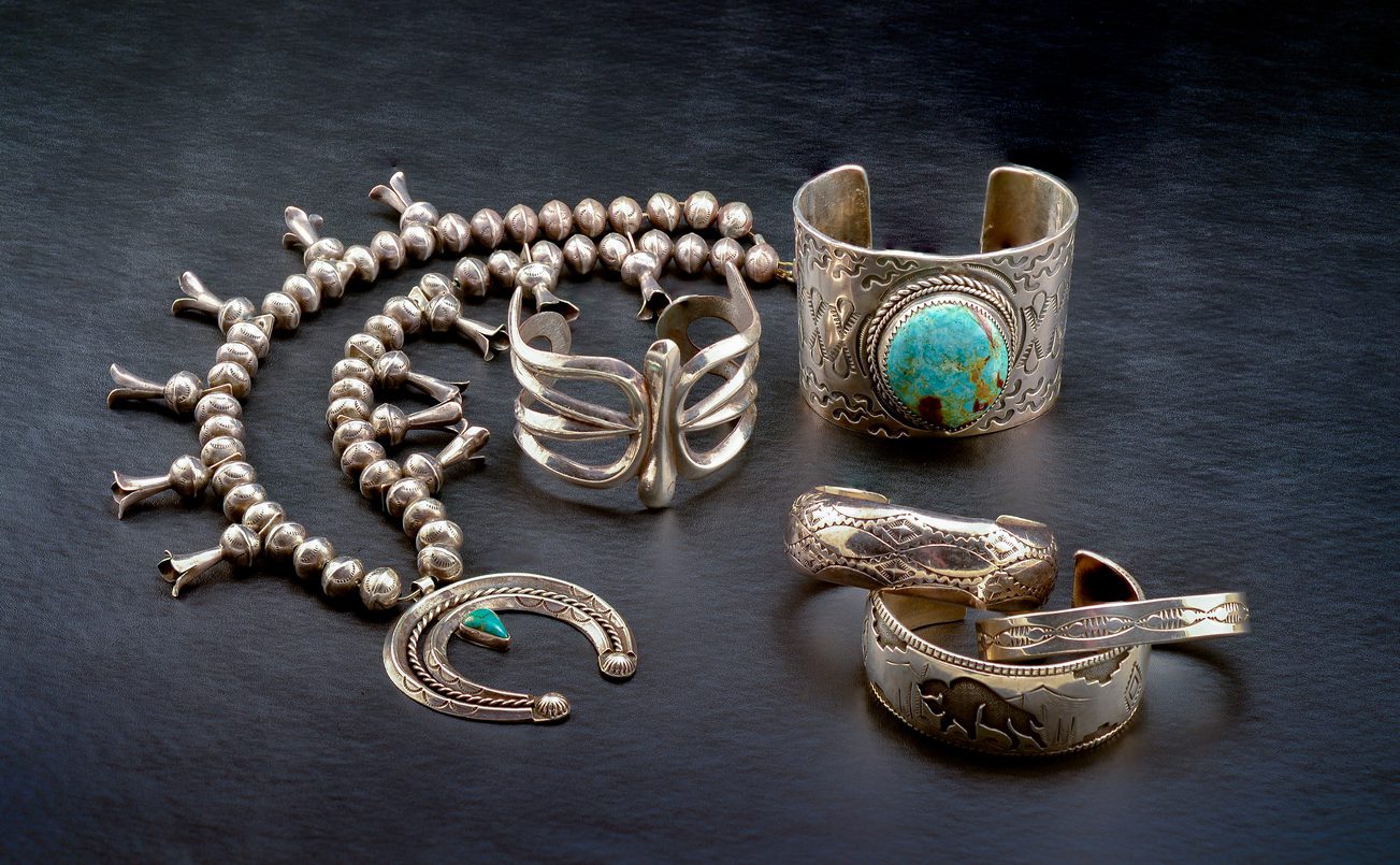 A Collection of Sterling Silver Native American Jewelry. Squash Blossom Necklace, Two Cuff Bracelets, One with a large Turquoise Stone, and Three smaller Bracelets.
